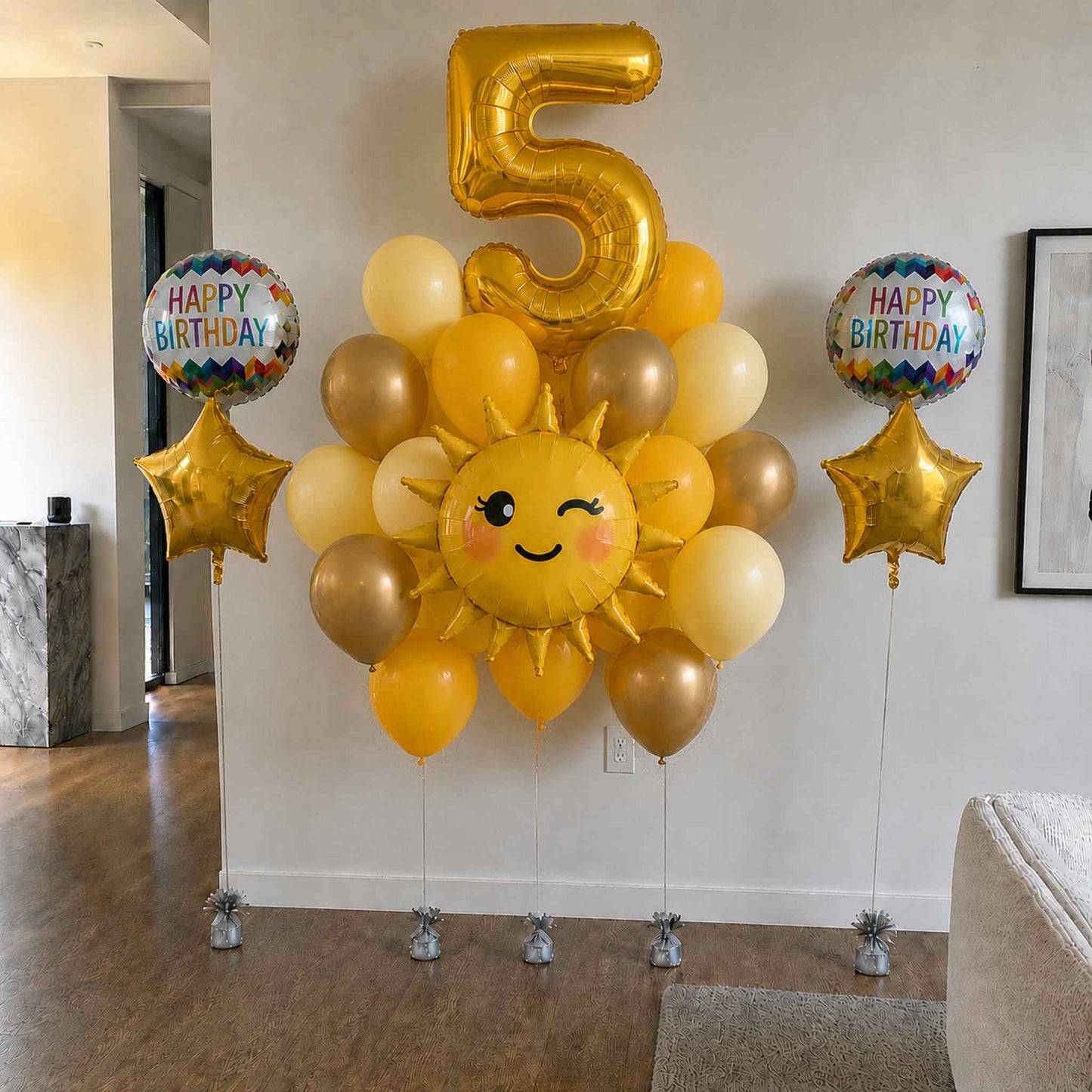 Balloon arrangement with a number 5 gold balloon, sun-shaped balloon, and 'Happy Birthday' balloons in a room.