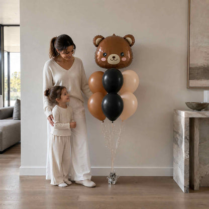 Woman and child standing next to a large teddy bear-shaped balloon in a living room.