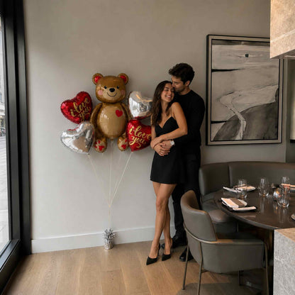 Couple standing in a modern dining area with balloons shaped like a teddy bear and heart.