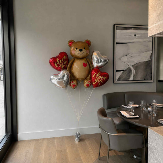 Teddy bear-shaped balloon with heart balloons in a dining area.
