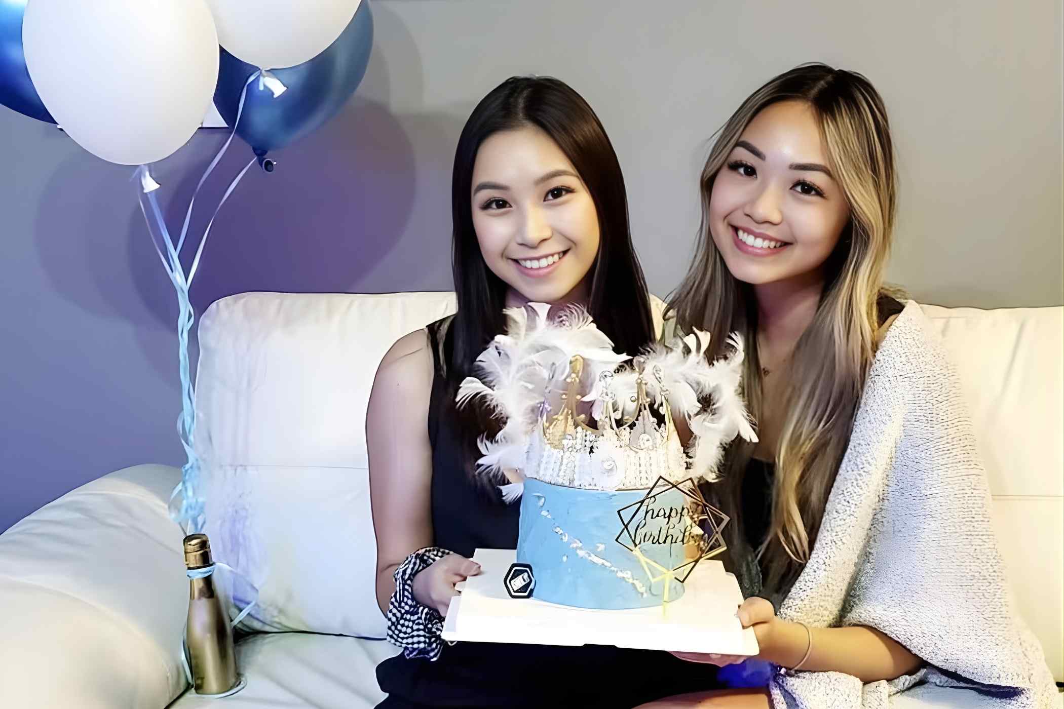 Two women sitting on a couch with a birthday cake and balloons in the background.
