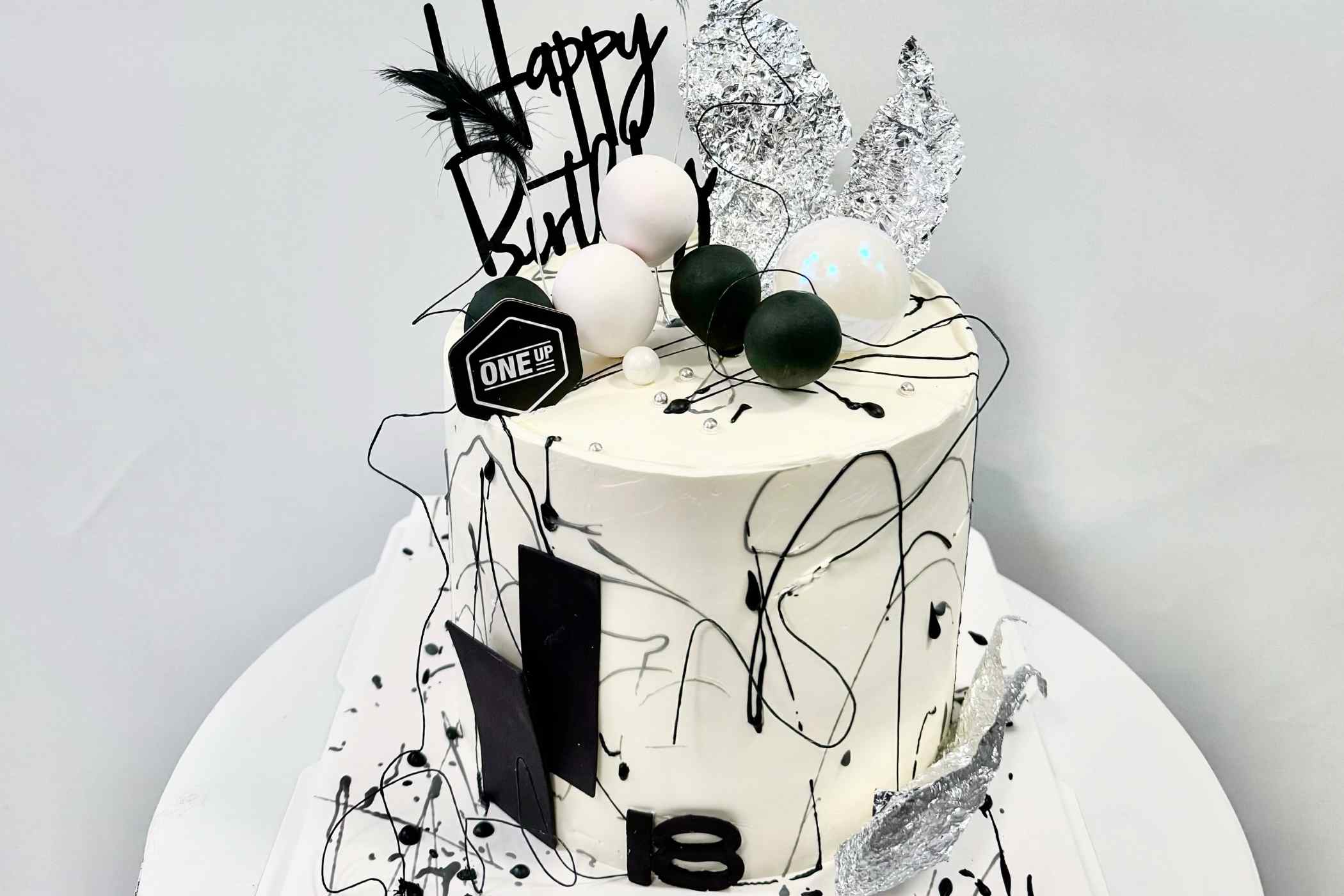 White birthday cake with black and gray decorations on a white plate against a light gray background