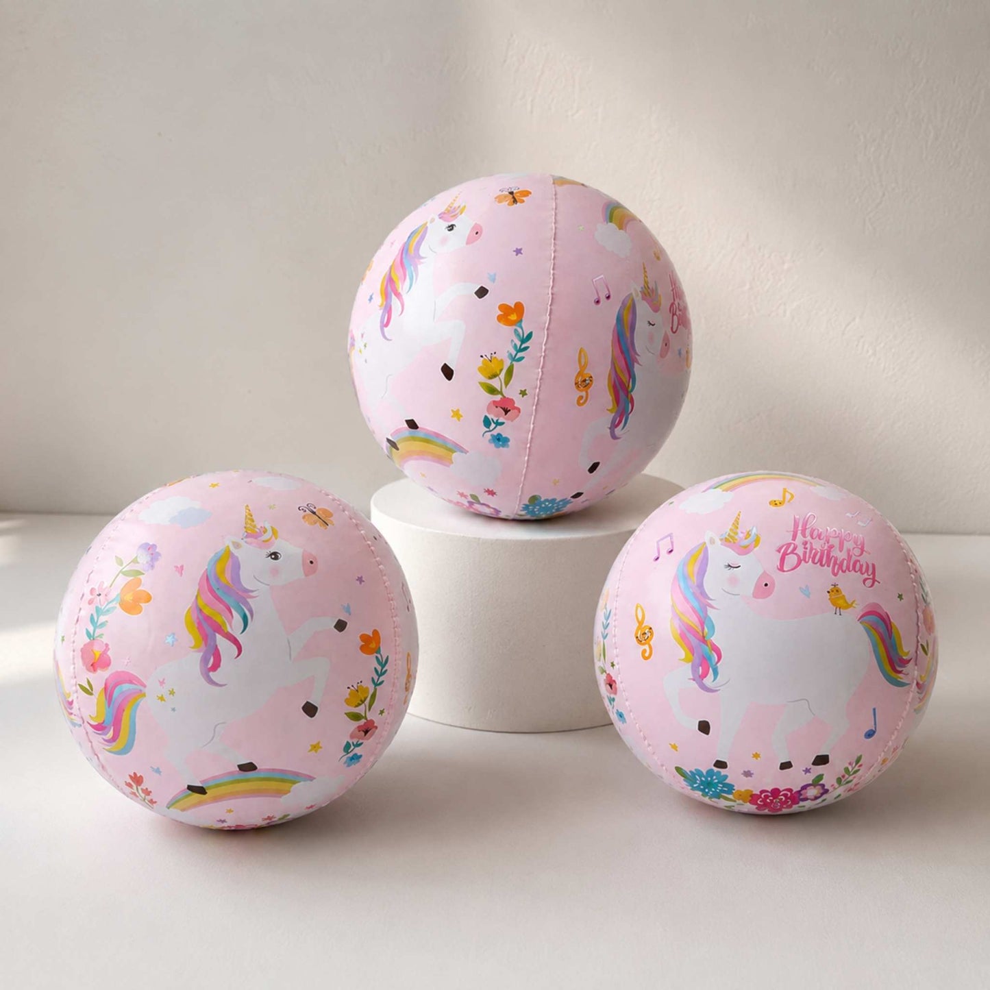 Three pink balloons with unicorn and rainbow designs on a white surface.