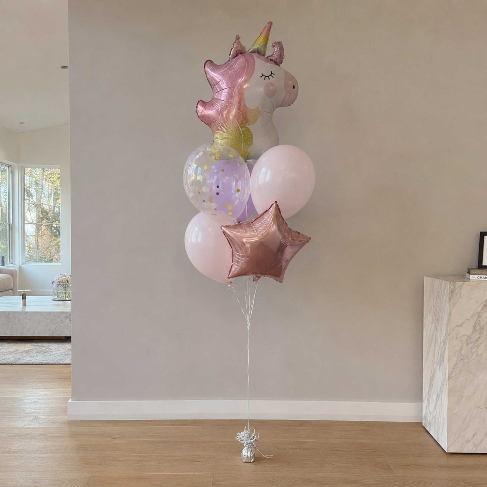 Bouquet of colorful balloons including a unicorn and star shapes in a room.