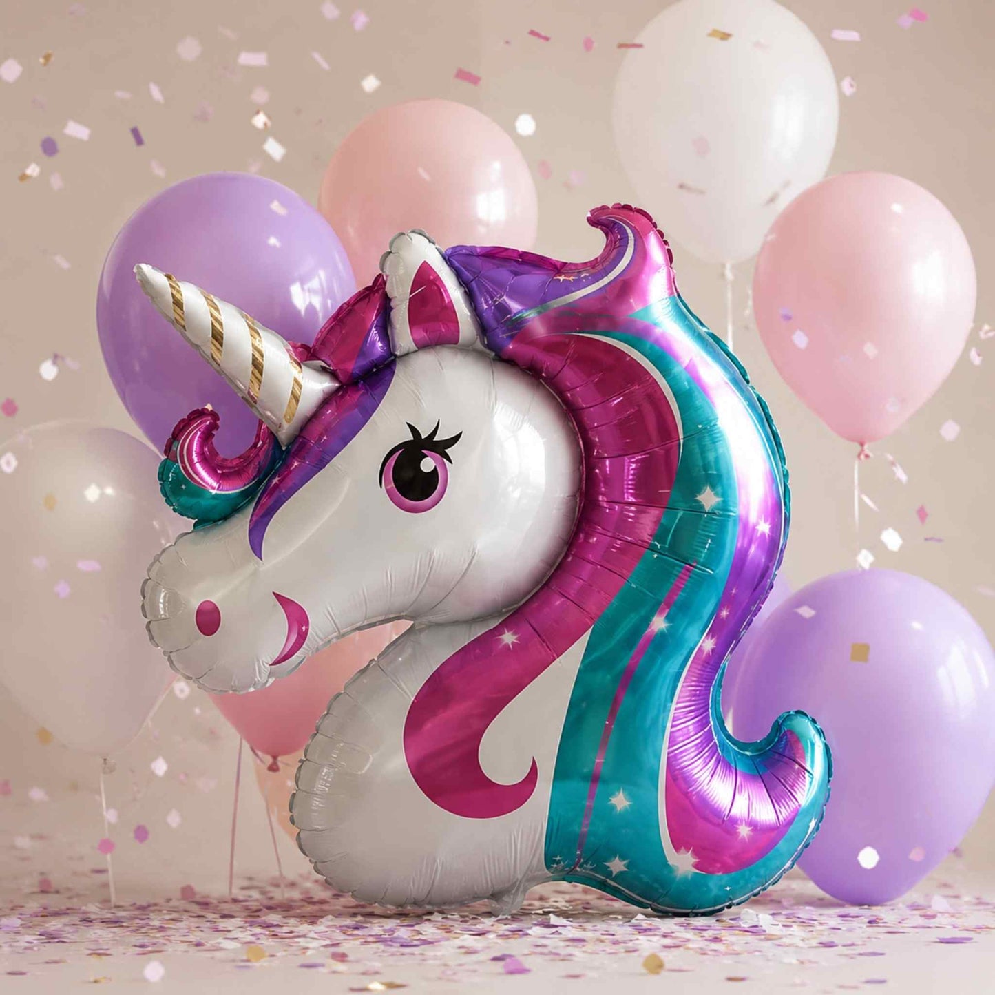 A metallic foil balloon shaped like a unicorn head is centered in front of pastel balloons and scattered confetti. The unicorn has a white face and body with a purple and teal mane, a gold-and-white horn, and small star details.