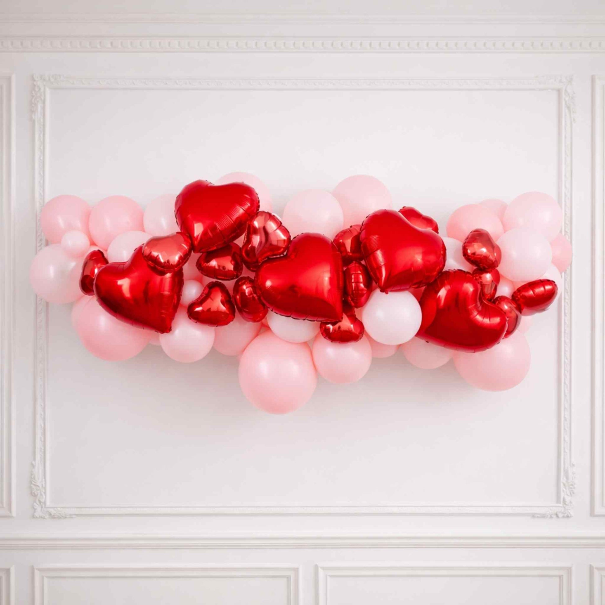 Heart-shaped balloons in red and pink on a white wall