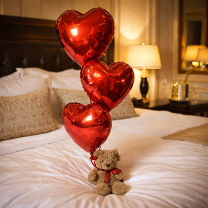 Teddy bear with red heart-shaped balloons on a bed in a bedroom setting