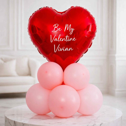 Red heart-shaped balloon with 'Be My Valentine Vivian' text on a white marble table.