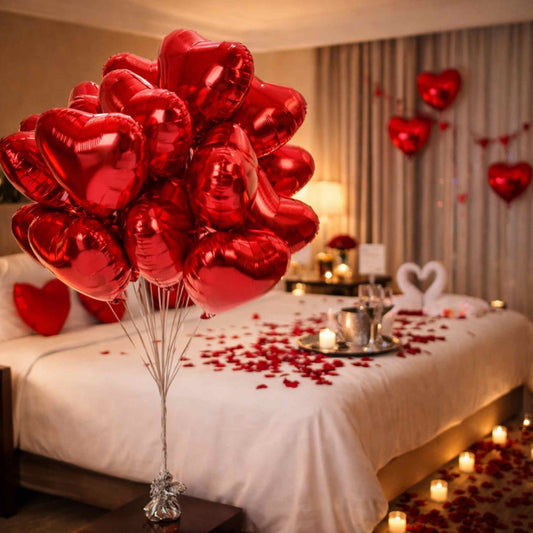 Red heart-shaped balloons on a bed with candles and rose petals in a romantic bedroom setting.
