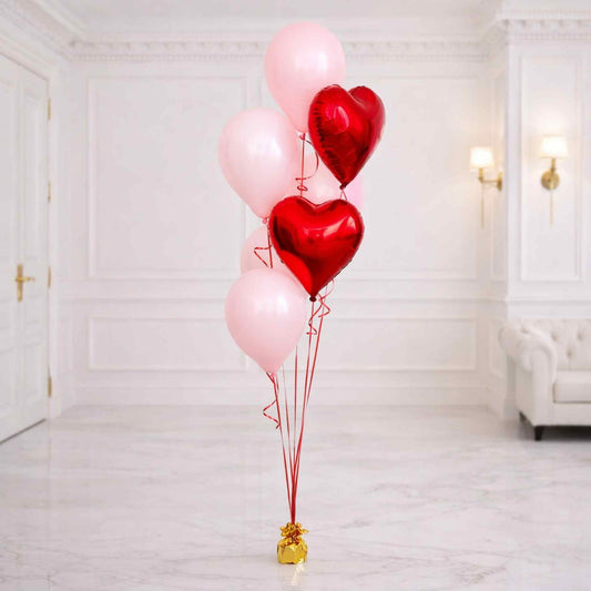 Red heart-shaped balloons tied together with pink ribbons in a room with white walls and a sofa.