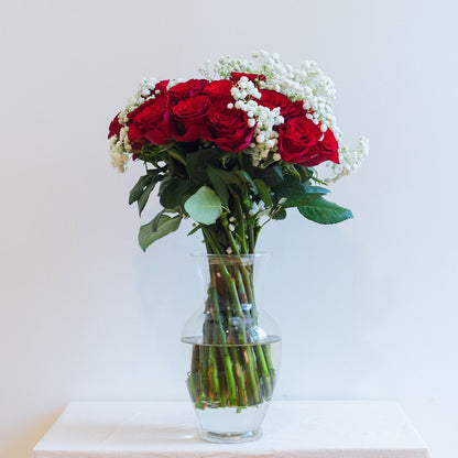 A bouquet of pink roses with white baby's breath fillers, placed in a clear glass vase.