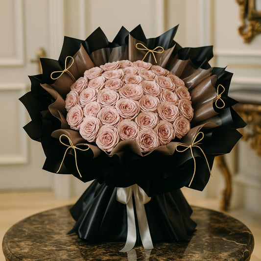 Bouquet of pink roses wrapped in black paper with gold ribbons on a marble surface.