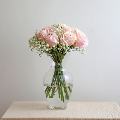 A bouquet of pink roses with white baby's breath fillers, placed in a clear glass vase.