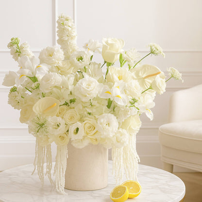 Bouquet of white flowers in a vase on a table with lemons, against a neutral background.