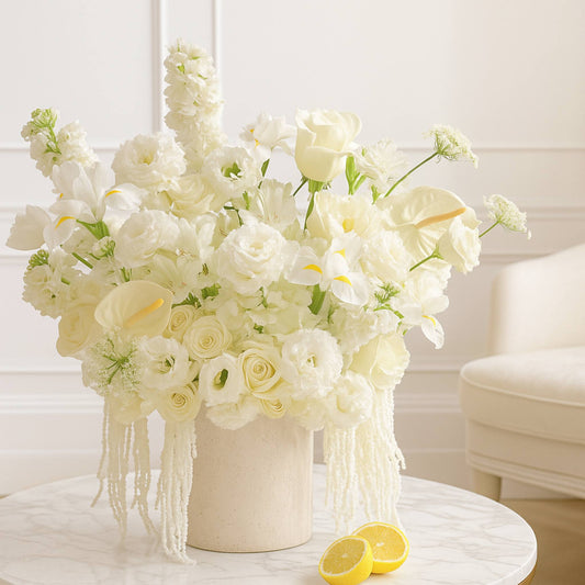 Bouquet of white flowers in a vase on a table with lemons, against a neutral background.