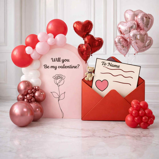 Valentine's Day-themed setup with balloons, a pink card, and a red envelope on a white marble surface.