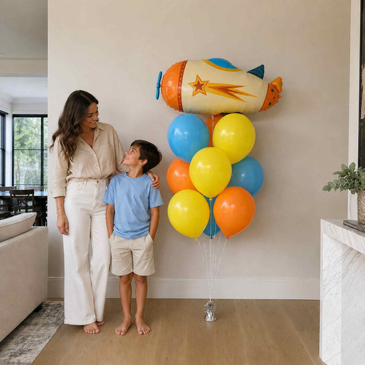 Woman and child standing next to a large cluster of colorful balloons shaped like a rocket.