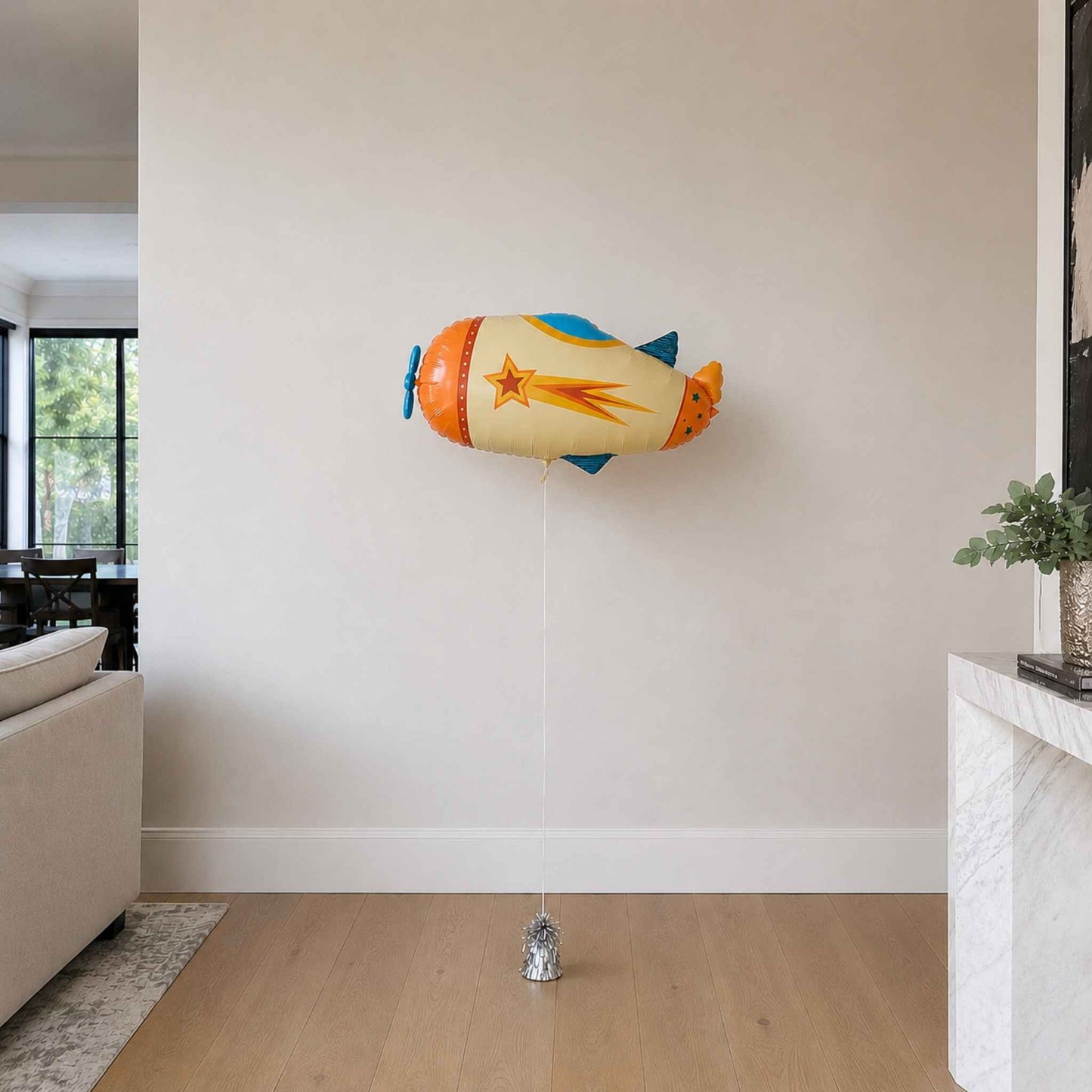 Colorful toy airship hanging on a wall in a room with a couch and plant.