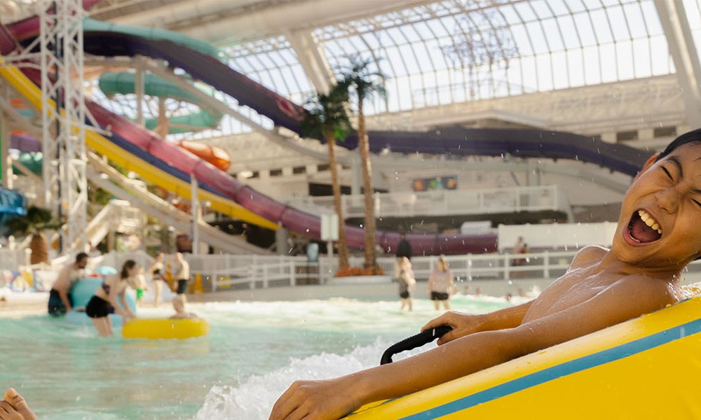 Person sliding down a water slide at an indoor water park with slides and pool in the background.