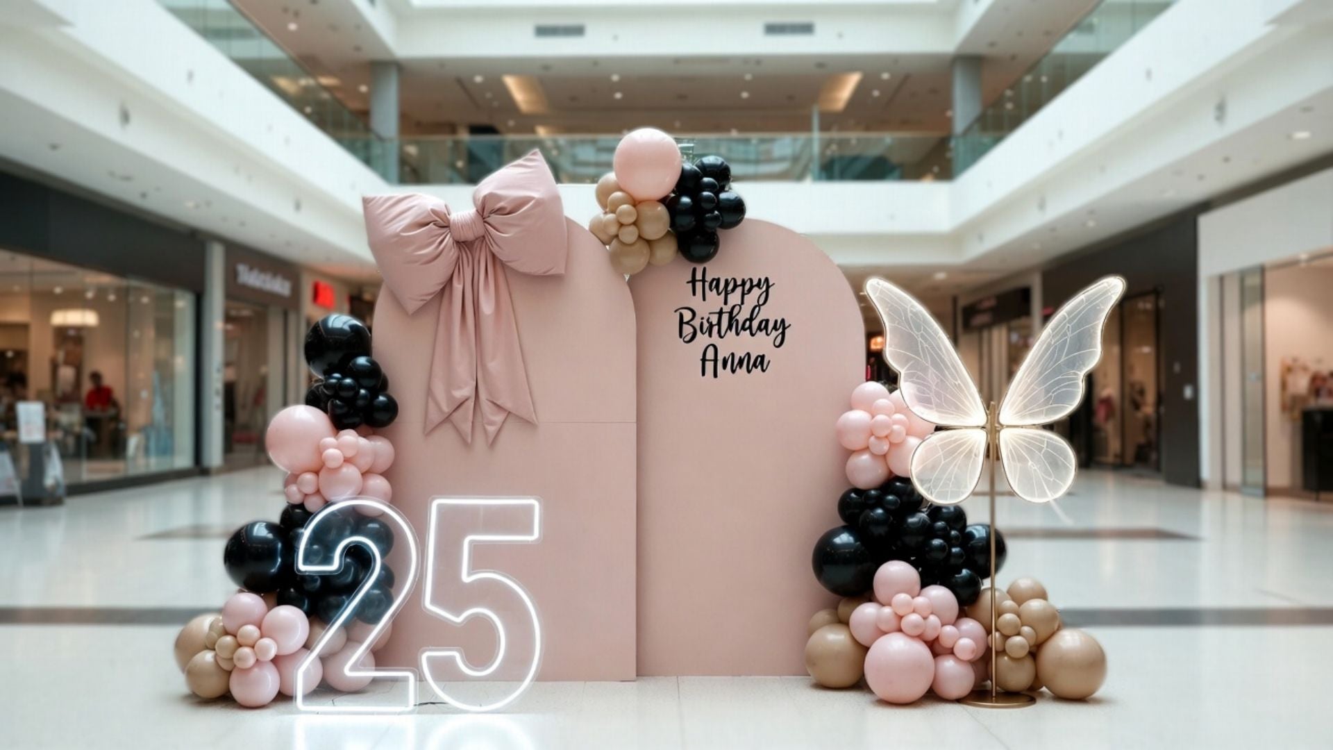 Birthday decoration arch with balloons and 'Happy Birthday Anna' text in a mall setting.