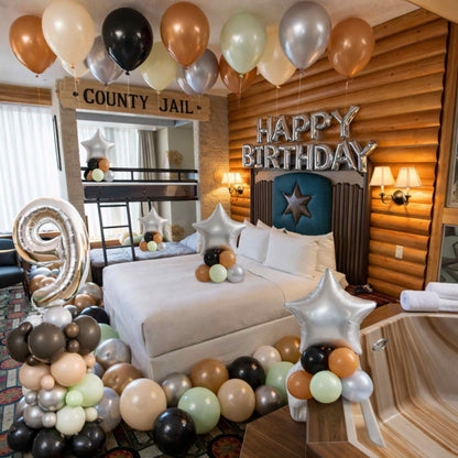 Decorated room with balloons and 'Happy Birthday' sign, featuring a bed and wooden walls.