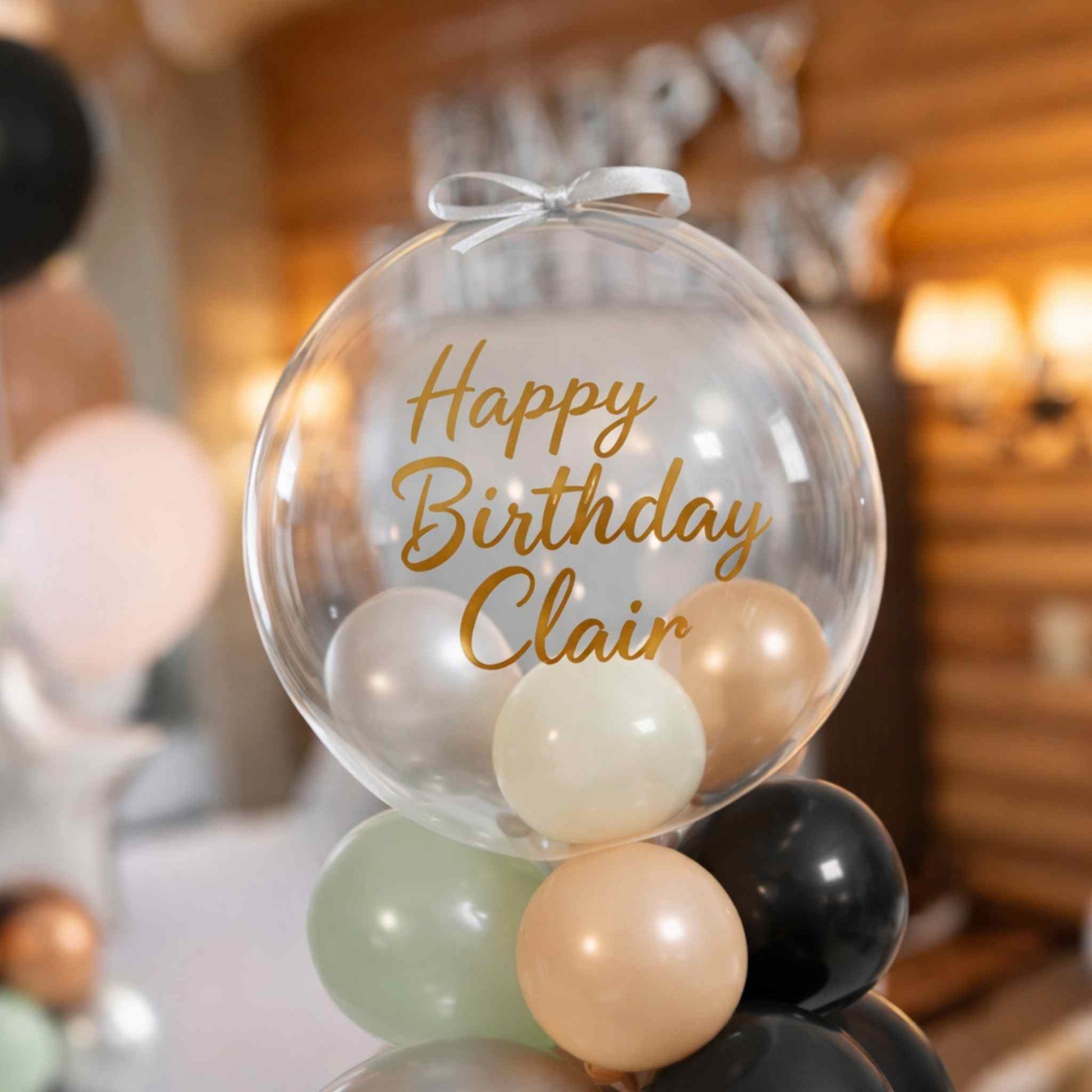 Clear balloon with 'Happy Birthday Clair' text and colorful balloons inside, blurred background