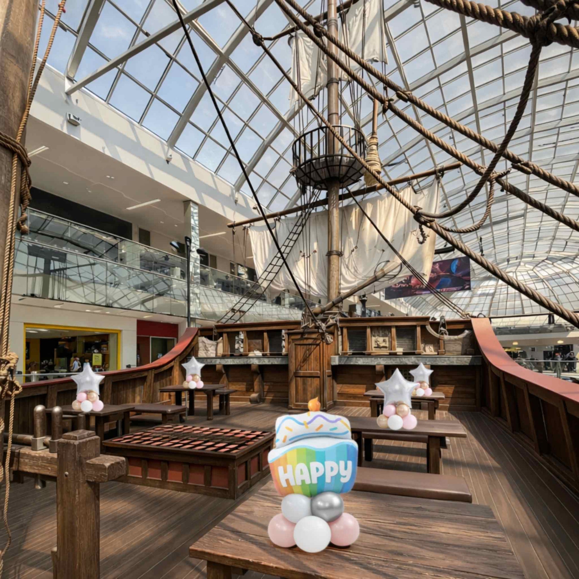 Large indoor ship model with a glass ceiling in a shopping mall setting.