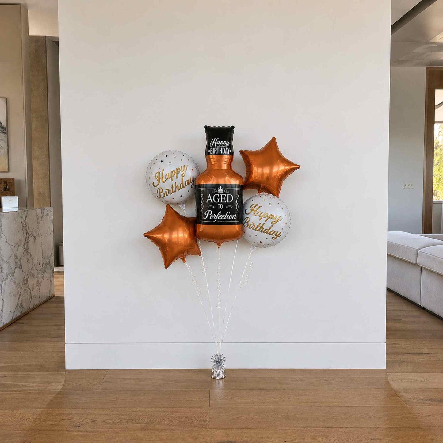 Balloon bouquet with 'Happy Birthday' and 'Aged to Perfection' text in a modern indoor setting.