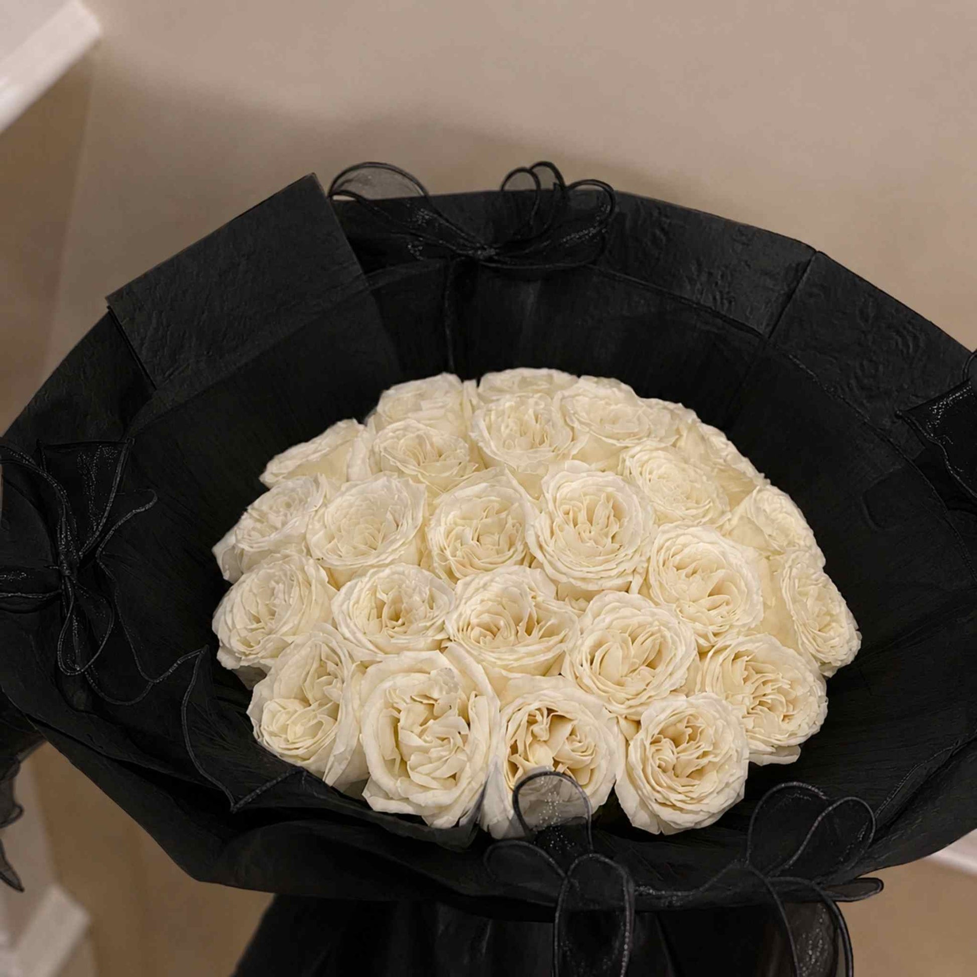 Bouquet of white roses in a black wrap with a neutral background