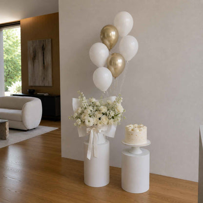 Decorative setup with balloons, flowers, and a cake in a room.