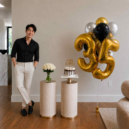 Man standing next to a cake and balloons with the number 35 in a room.