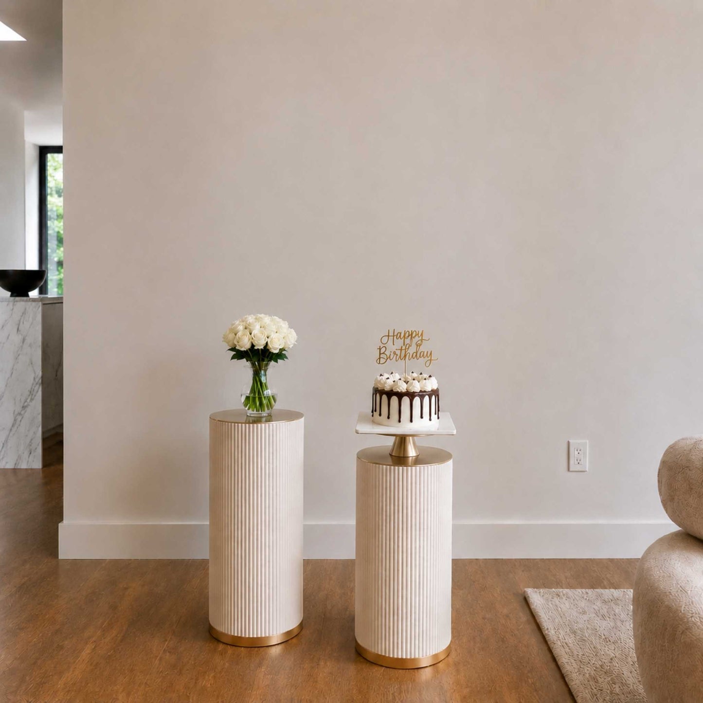 Small round table with a birthday cake and flowers in a room with a neutral color scheme.