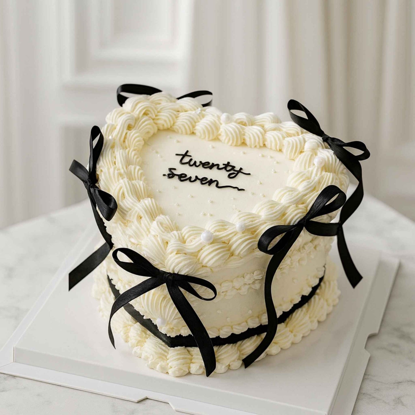 White cake with black ribbons and 'twenty seven' text on a marble surface.