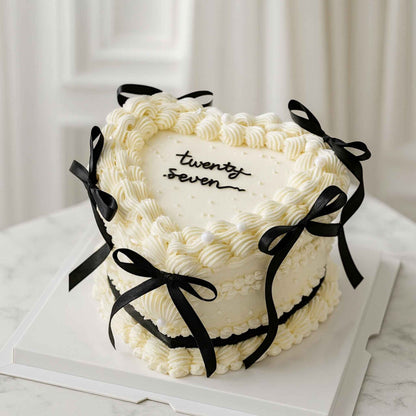 White cake with black ribbons and 'twenty seven' text on a marble surface.