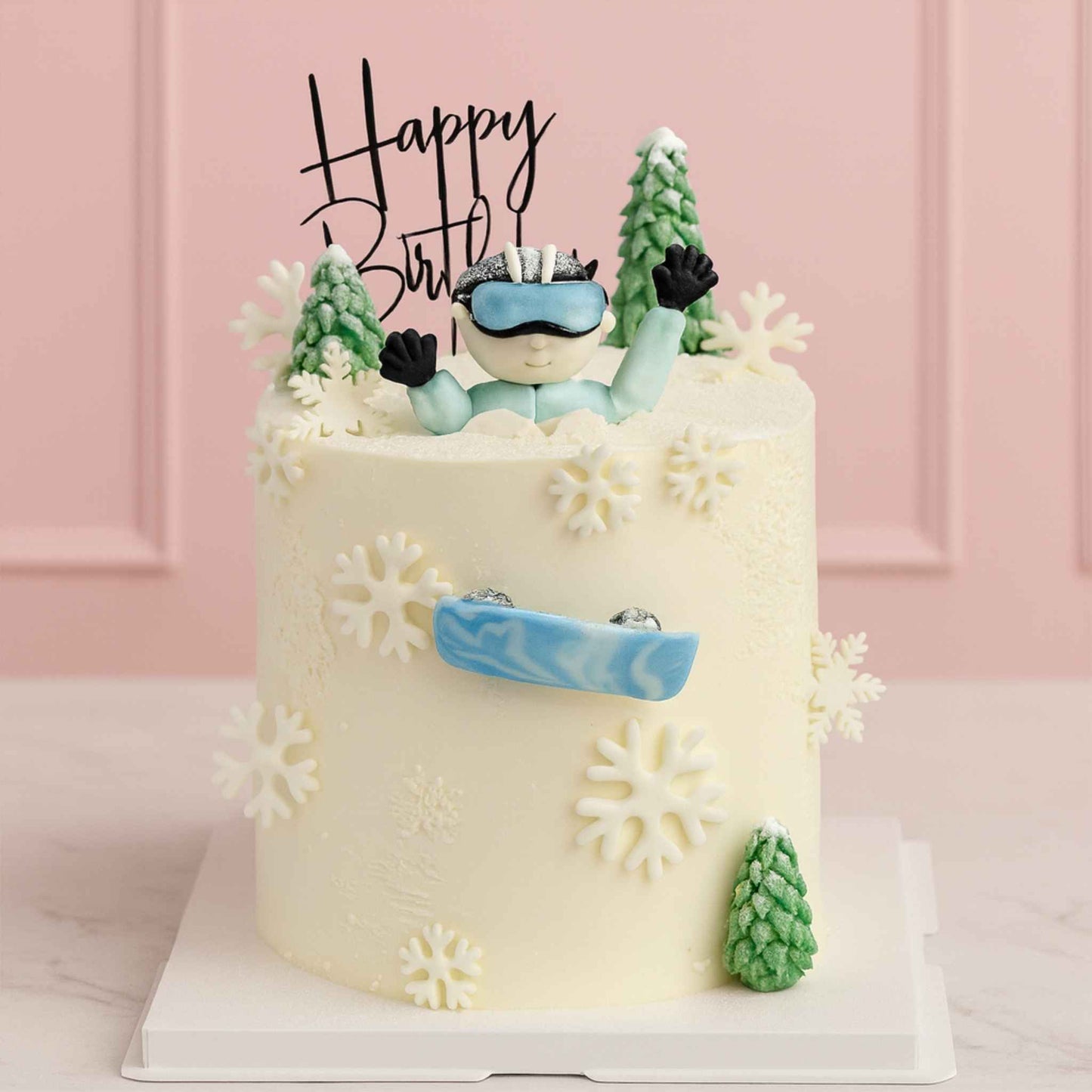 Birthday cake with skier figurine and snowflake decorations against a pink background
