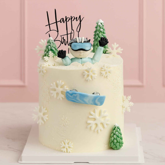 Birthday cake with skier figurine and snowflake decorations against a pink background