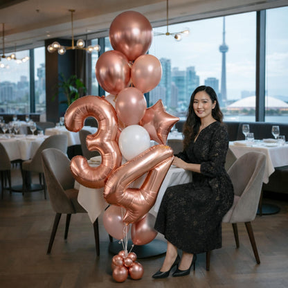 Woman sitting at a table with a large bouquet of rose gold balloons shaped like the number 34 in a restaurant setting.