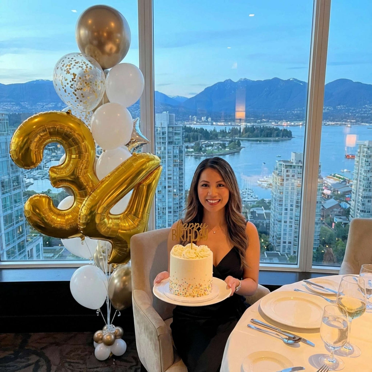 Woman holding a cake with balloons and a scenic city view in the background