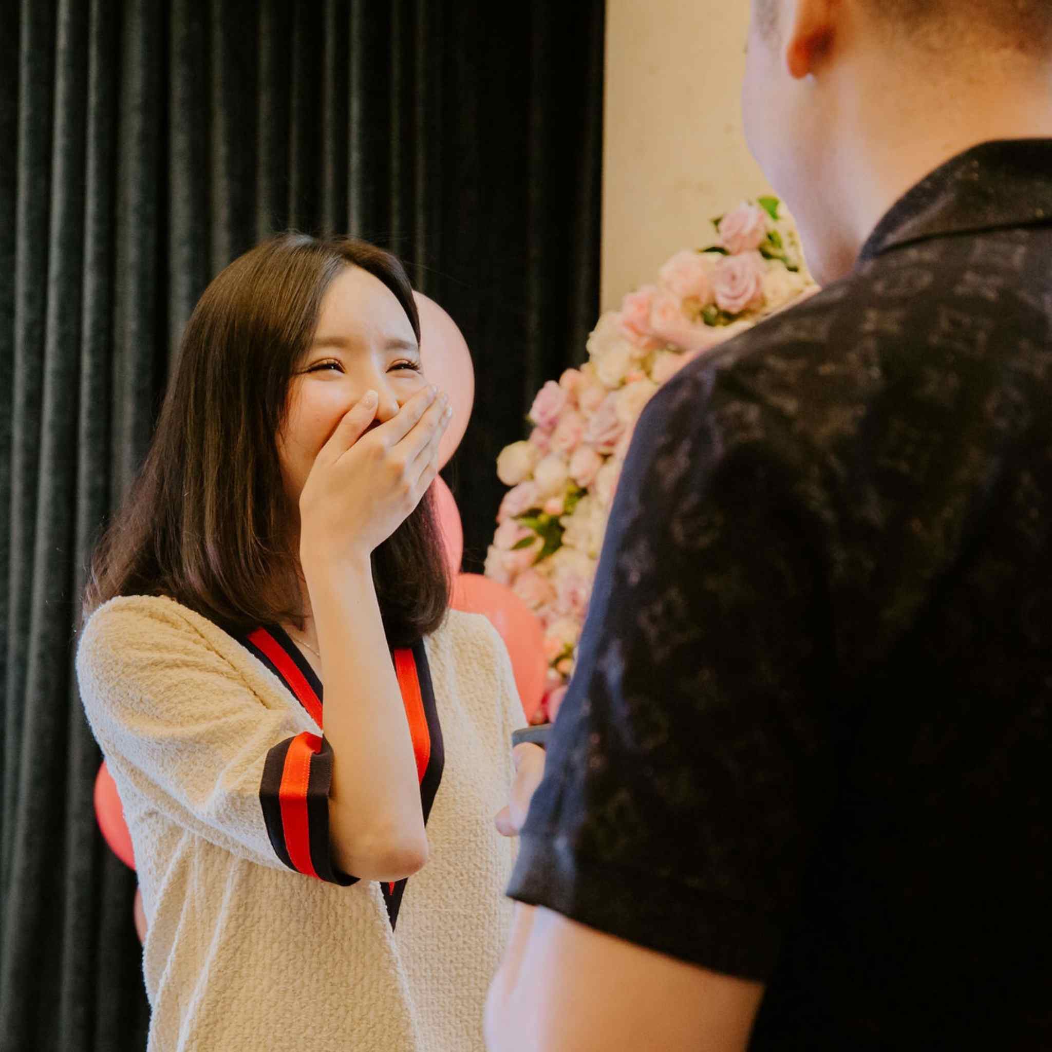 Woman reacting with surprise to a man with flowers behind her