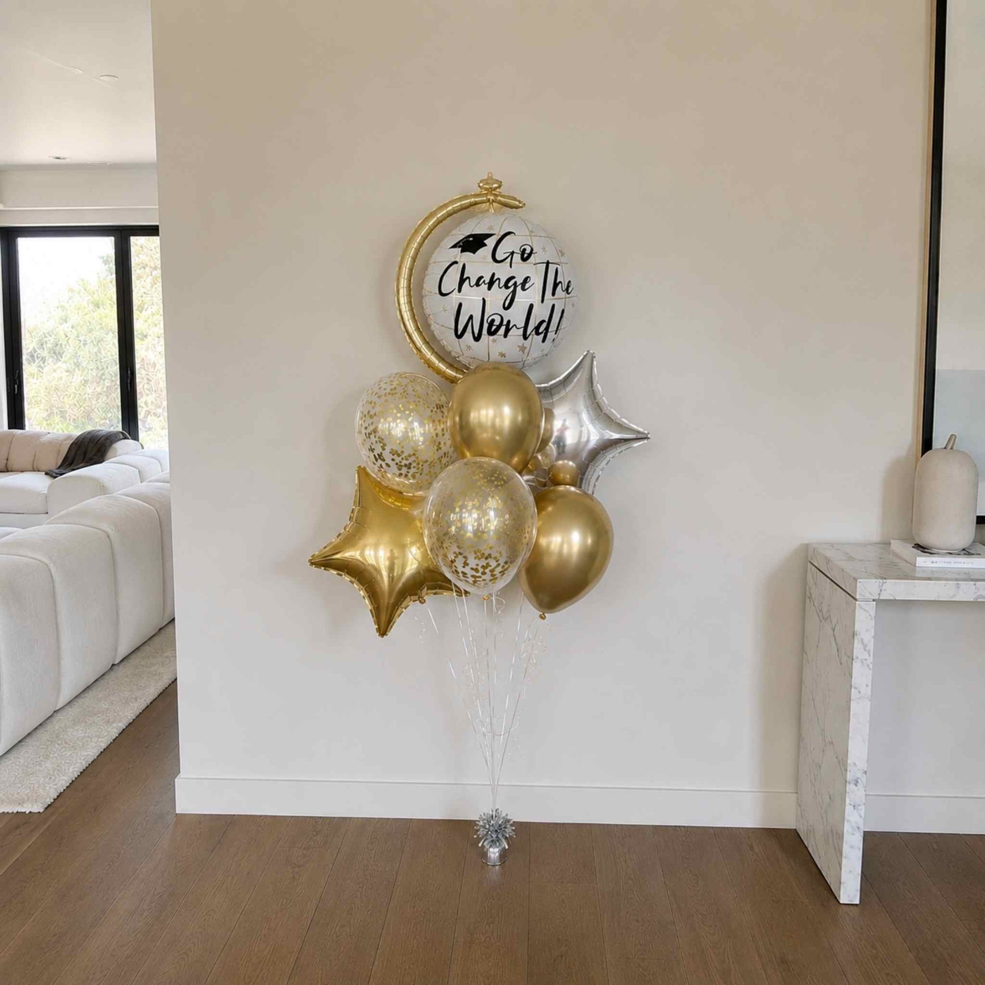 Decorative balloon bouquet with gold and silver balloons against a white wall in a living room.