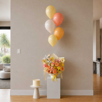 Decorative arrangement with balloons, flowers, and a cake in a room.