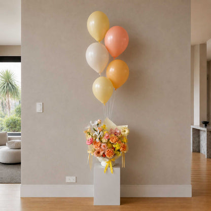 Bouquet of flowers with colorful balloons on a pedestal against a beige wall.