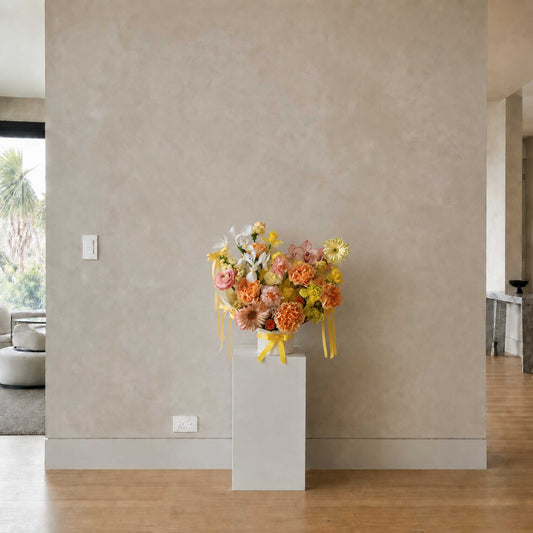 Bouquet of flowers on a white pedestal against a beige wall.
