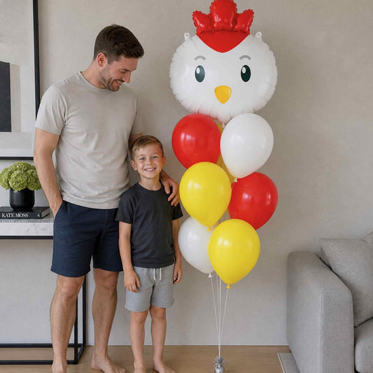 Man and child standing next to a large balloon shaped like a chicken with red, yellow, and white balloons.